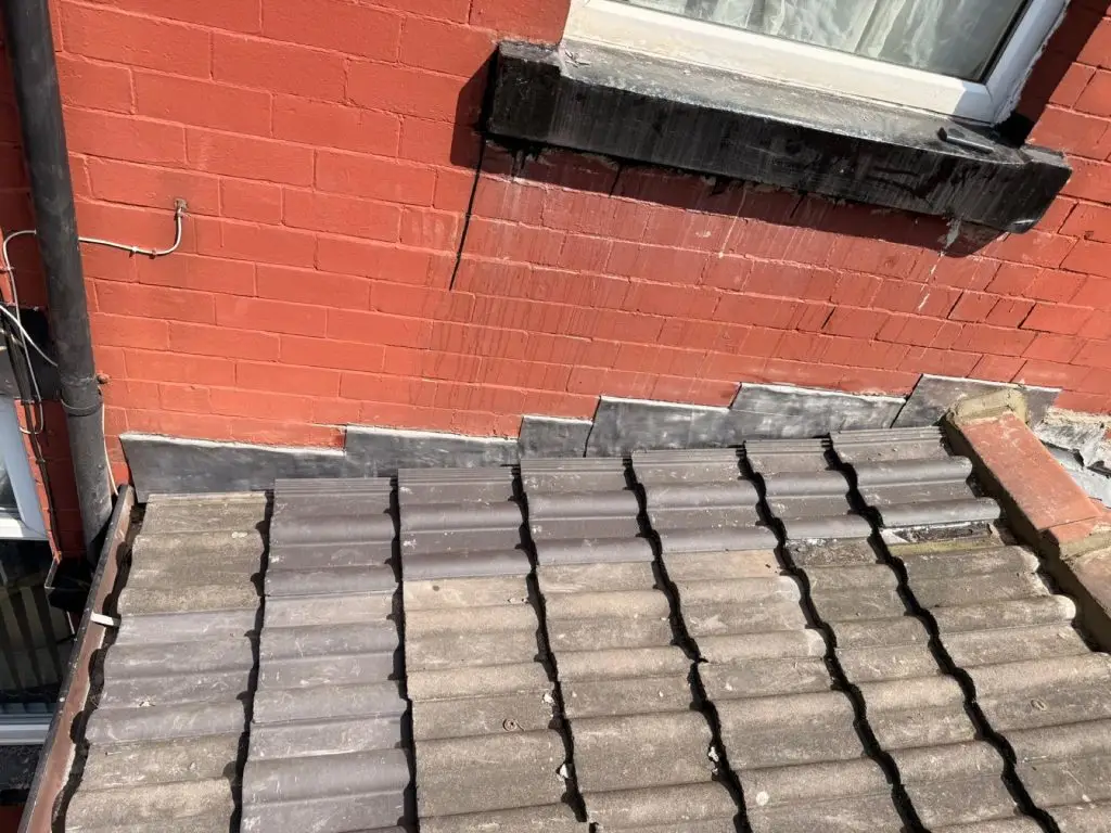 Concrete tile roof with fresh lead flashing dressed into the brickwork of a red-painted Leeds terrace extension.