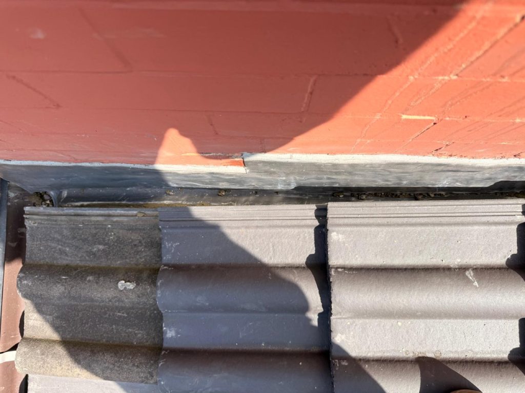 Close-up of fresh lead step flashing tucked above interlocking concrete roof tiles.