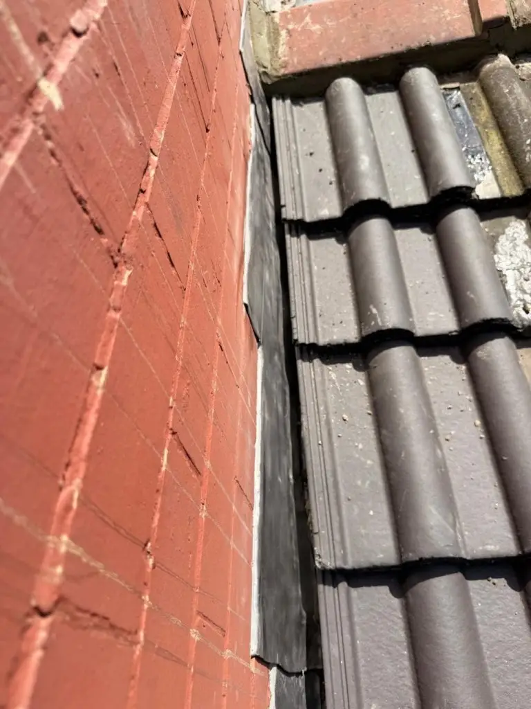Tight detail of new sand-and-cement pointing along the wall-to-tile junction with crisp lead flashing.
