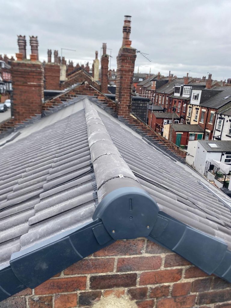 Pristine new charcoal-grey roof with fresh ridge tiles running away over a Leeds terraced street, brick chimneys lining the skyline.