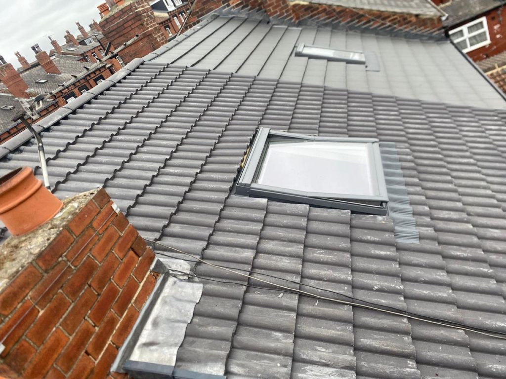 Roof-level view of a new charcoal roof with two Velux skylights, an old red brick chimney to the side.