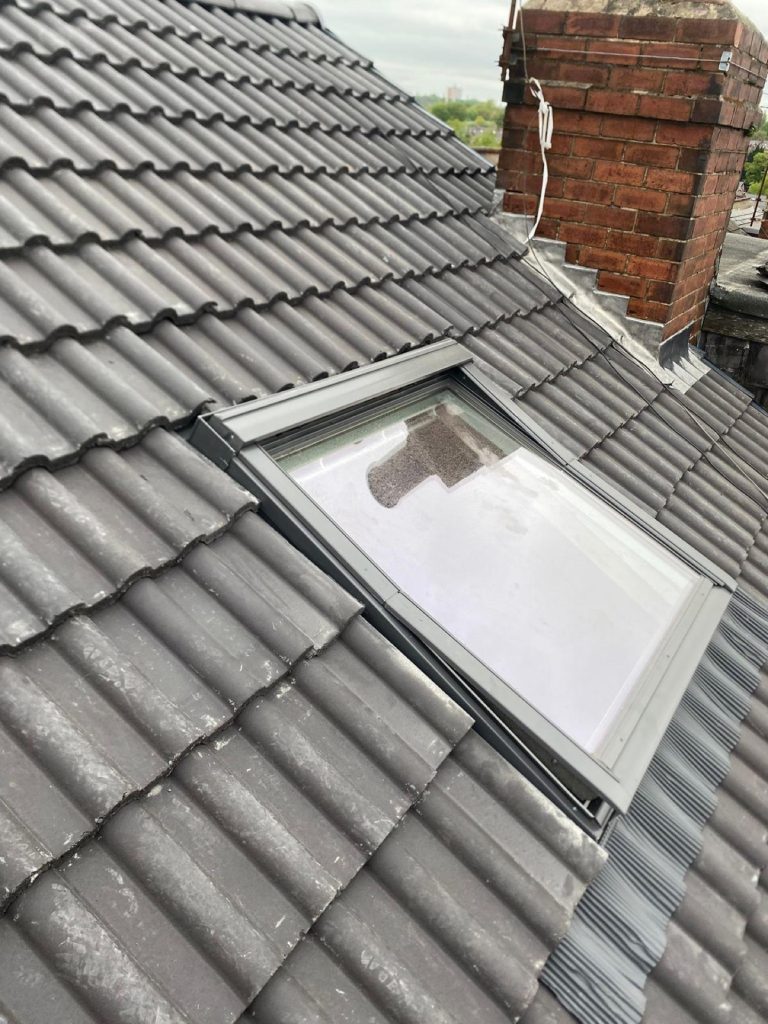 Close detail of a Velux skylight installed flush into a brand new charcoal tile roof, brick chimney to the side.