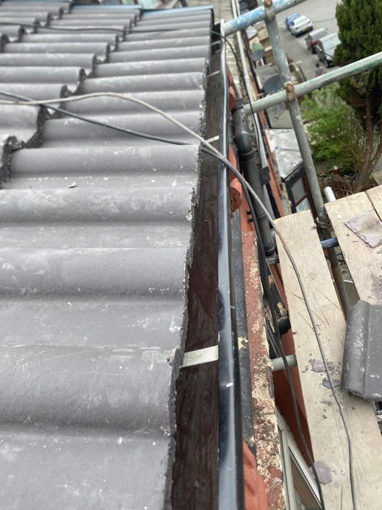 Close-up of the eaves edge with new tiles and pointing alongside scaffolding above a Leeds residential street.